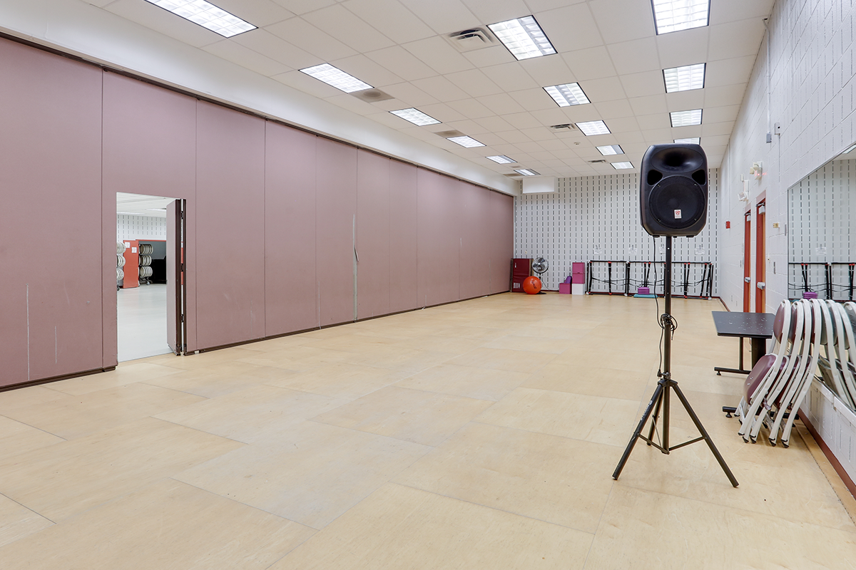 A large multipurpose room with a room divider separating a section with a mirrored wall and a wooden dance floor.