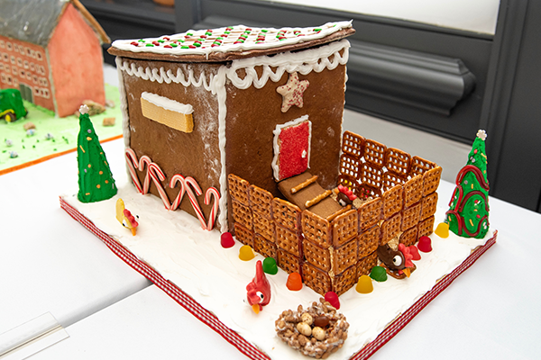 A gingerbread chicken coop with candy cane and chocolate decorations. Off of the one side, a large open area fenced in by pretzels lets the chocolate chickens roam around at their leisure.