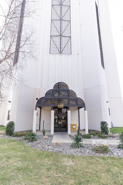 Exterior view of the base of a white water tower with a tiered, smoked-glass portico over the entrance.