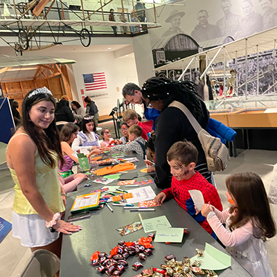 Woman handing out candy at a table to kids dressed in Halloween costumes
