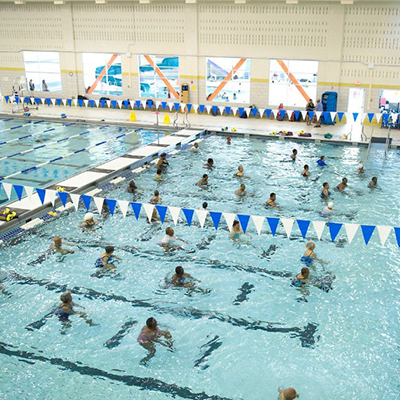Dozens of people swimming in a pool with blue and white pendants overhead