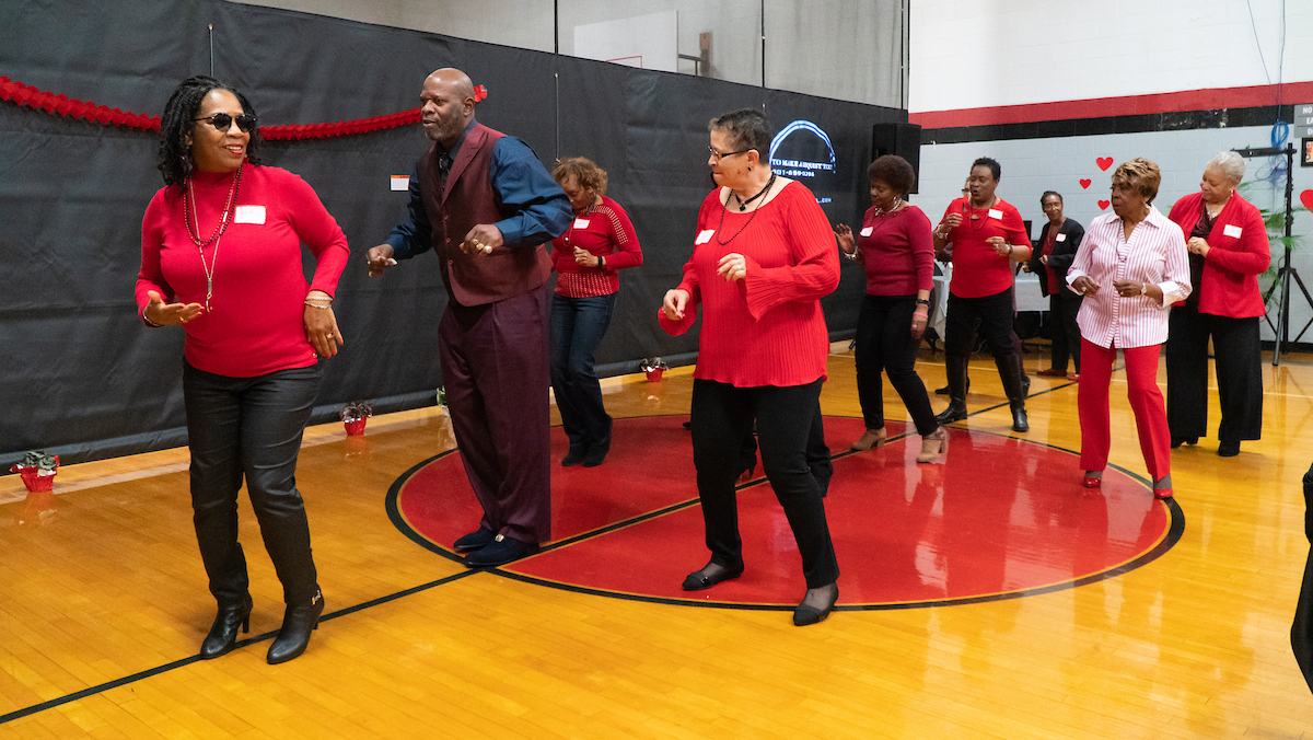 Inside a gymnasium decorated for Valentine's Day, about a dozen seniors wearing red dance in formation near the DJ booth.