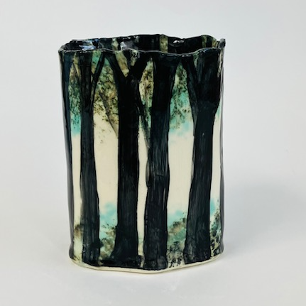 A cylindrical ceramic vase painted with dark, silhouetted trees against a pale background.