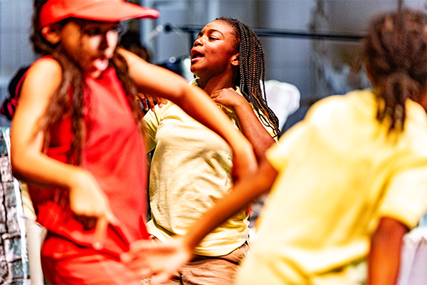 Three girls dancing. There are two wearing yellow shirts, and one wearing a red shirt.