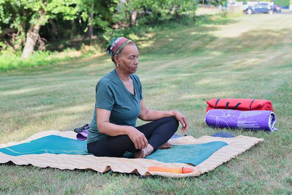 A woman calmly meditating in a blanket in a grass field.