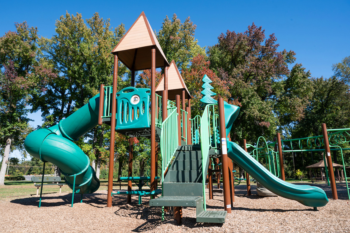 A playground with a large play structure featuring slides, platforms, towers, stairs, monkey bars, and benches. A picnic shelter is nearby.