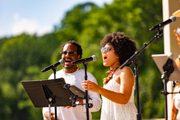 A man and a woman singing into microphones outdoors.