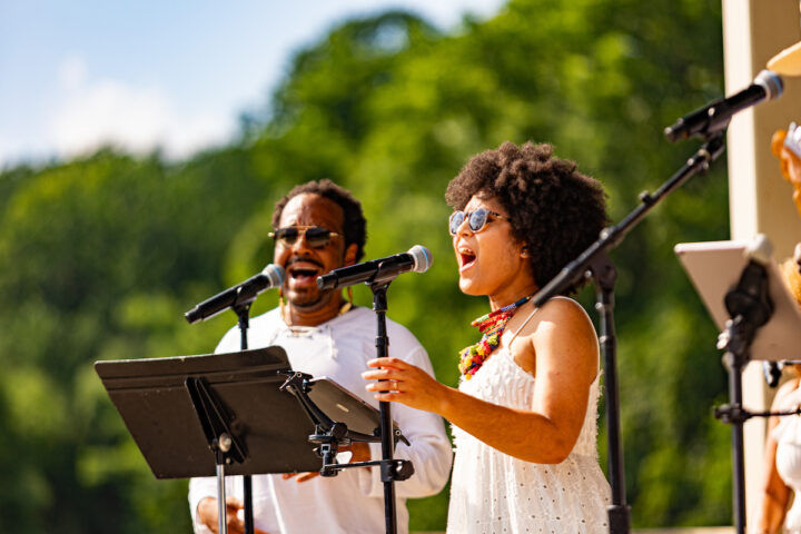 A man and a woman singing into microphones outdoors.