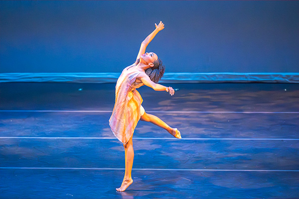 A woman dances barefoot on a stage, making an arabesque-like pose.