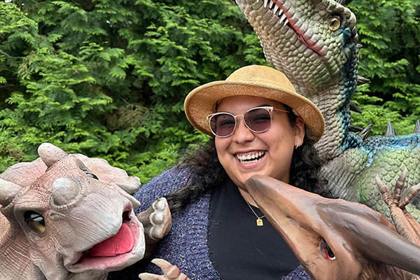 A laughing woman poses with several large, detailed dinosaur puppets.