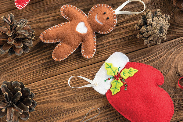 Holiday ornaments made of felt on a table with some pinecones.