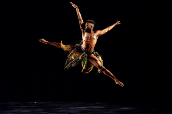 Male dancer in a costume with feathers jumps and dances on stage.
