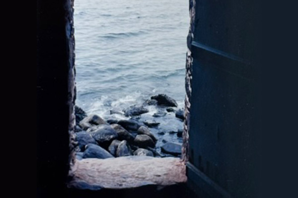 Waves of water lapping up on rocks, seen through a rough stone window.