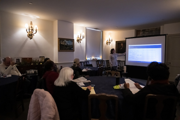 Participants attend a genealogy workshop, watching a presenter explain research tools on a projected screen.